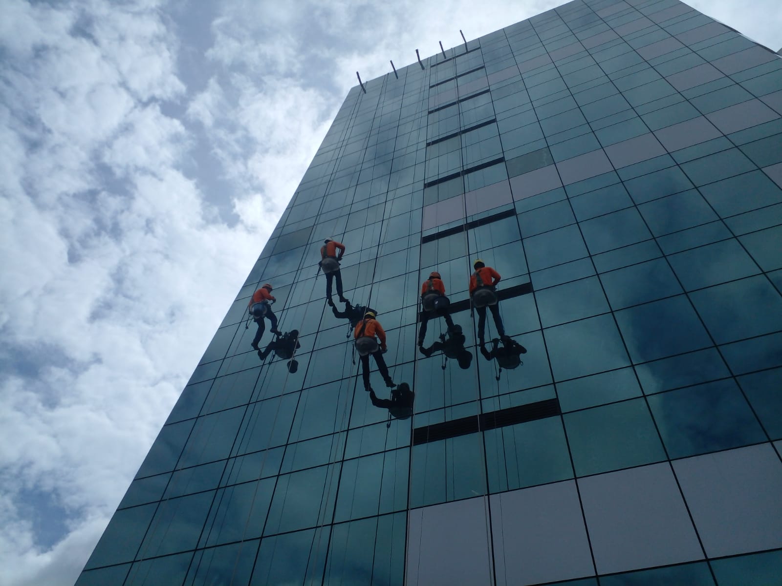 Equipe da ENGECRON realizando limpeza de fachada de vidro em rapel em edifício comercial